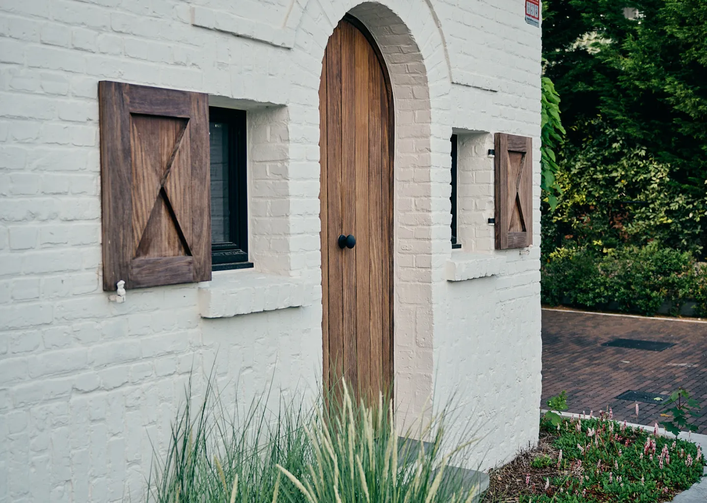 Siergrassen voor de ronde houten voordeur van een Koksijdse villa door Tuinen Cobbaert